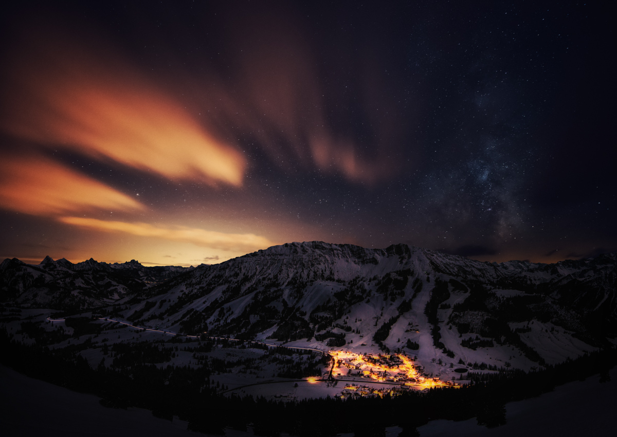 Milchstraße über beleuchteter Winterlandschaft Oberjoch, Allgäuer Alpen bei Nacht, Bergdorf unter dem Sternenhimmel
