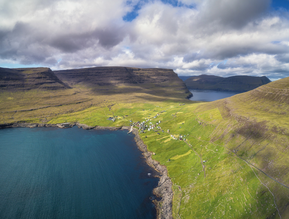Färöer Dorf, Kleines Dorf im grünen Tal zwischen Tafelbergen am Fjord, Idyllische Küste - Drohnenfotografie Nordatlantik