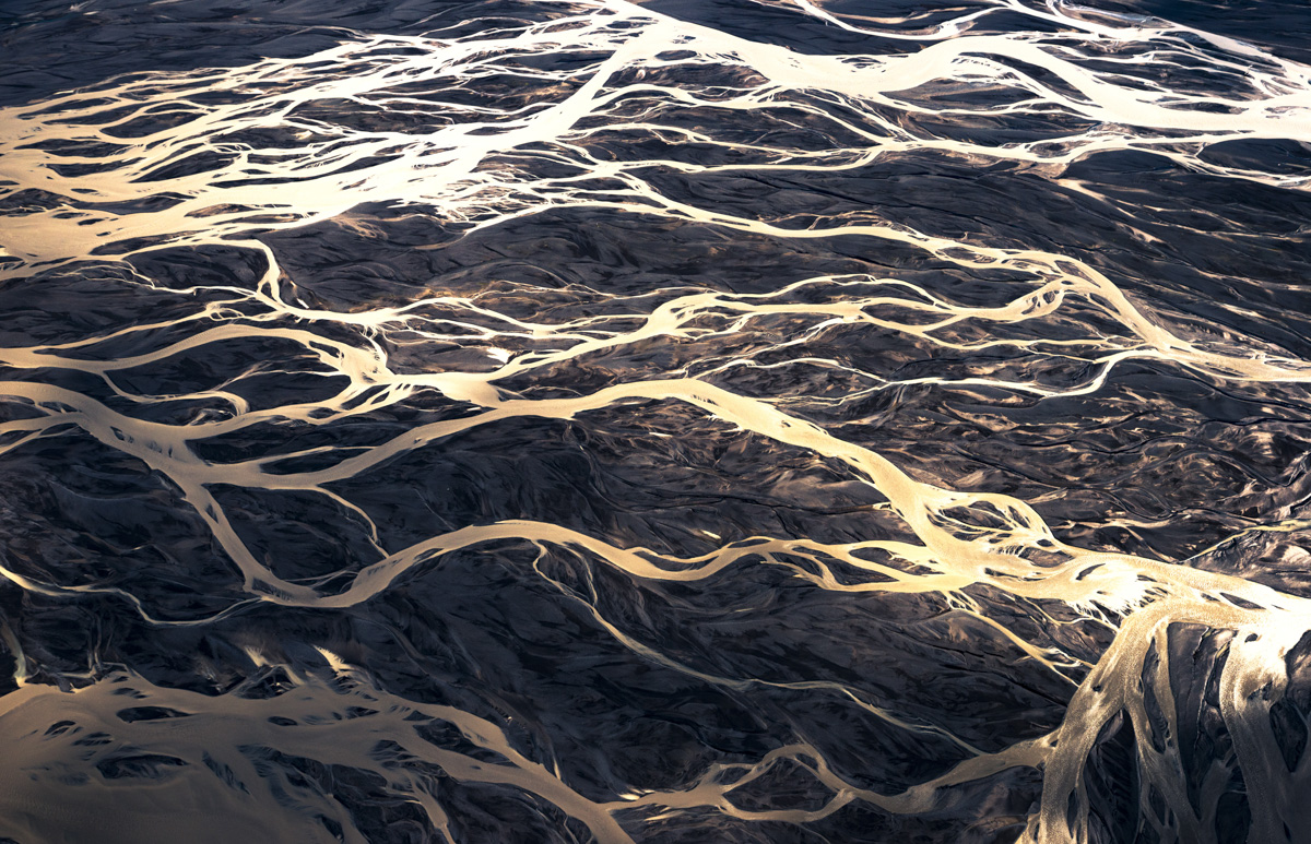 Gletscherfluss-Adern, Weiß-goldene Ströme auf nachtblauem Vulkansand, Abstrakt - Aerial Fotografie Island