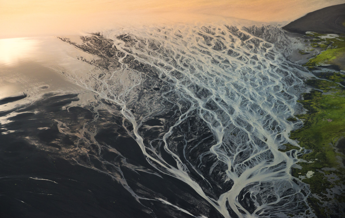 Gletscherfluss mündet ins Meer, Verzweigtes Delta auf schwarzem Sand bei Sonnenuntergang, Episch - Aerial Fotografie Island