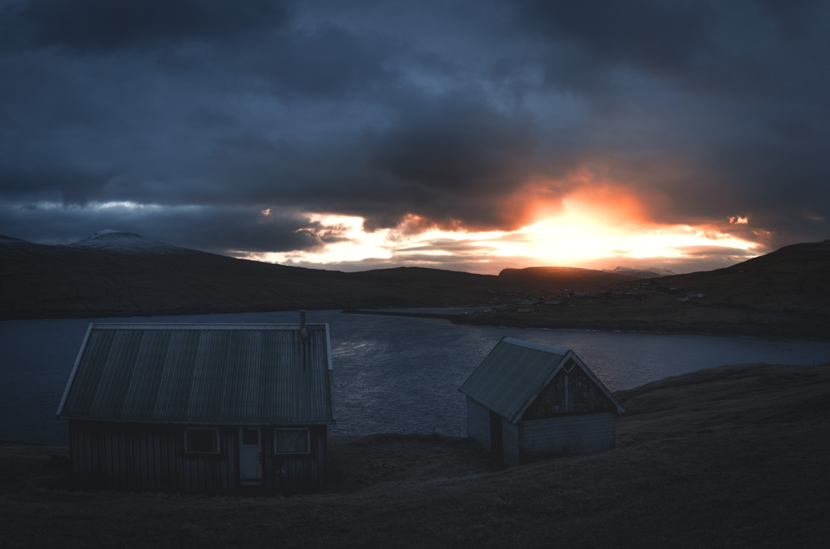 Färöer Hütten, Holzhütten am Fjordufer bei dramatischem Sonnenuntergang durch Wolkenbruch, Abendglut - Landschaftsfotografie