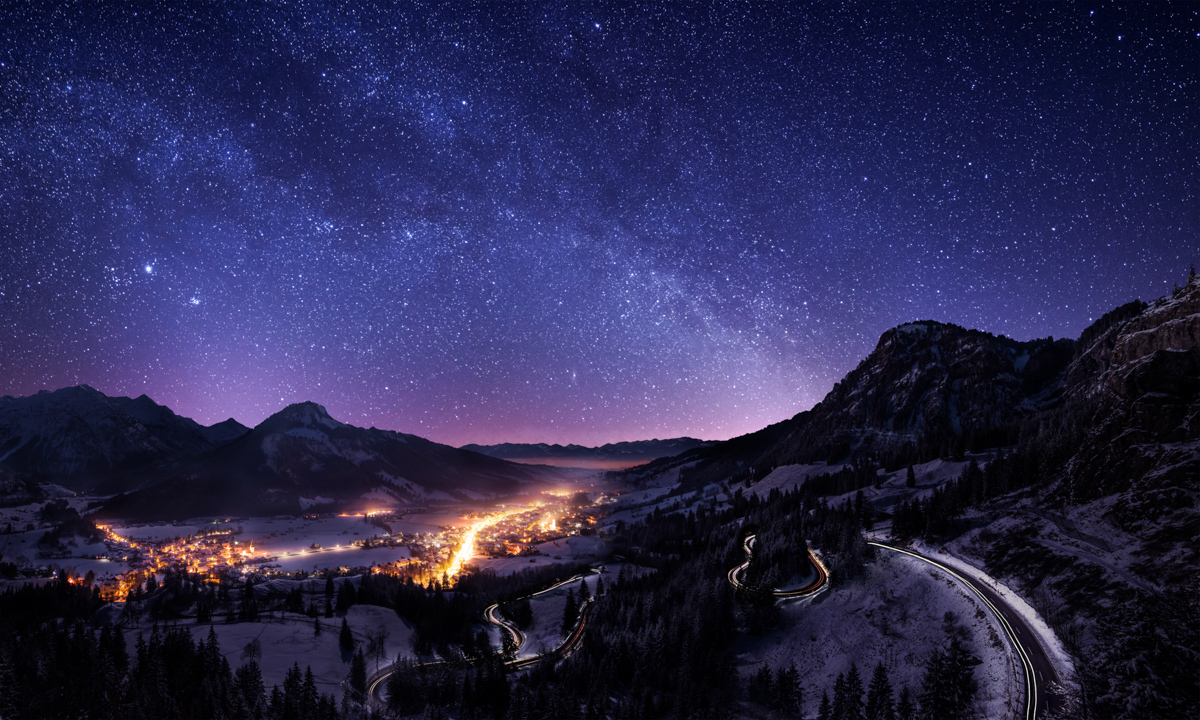 Milchstraße über dem Jochpass, Beleuchtetes Hindelang und Serpentinen vom Oberjoch bei Nacht, Panoramische Winterlandschaft