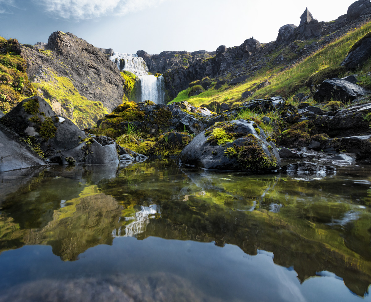Isländischer Wasserfall mit Spiegelung, Moosbedeckte Felsen im Gegenlicht, Idyllische Naturszene Island