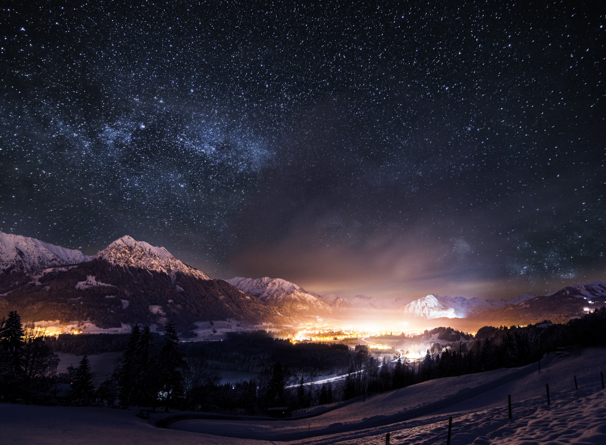 Winternacht über Oberstdorf, Milchstraße über verschneiten Bergen mit goldenen Stadtlichtern, Magische Sternenlandschaft