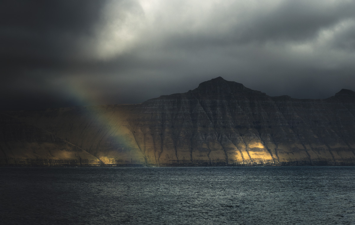 Färöer Inseln, Goldener Lichtstrahl auf Basaltbergwand am Fjord, Dramatisches Wettertheater - Landschaftsfotografie