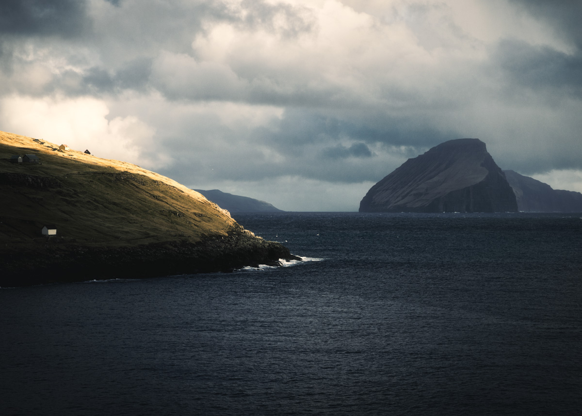 Färöer Inseln, Sonnenbeschienene Küste mit Basaltinsel im Gewitterhimmel, Kontrastreiche Fjordlandschaft - Naturfotografie