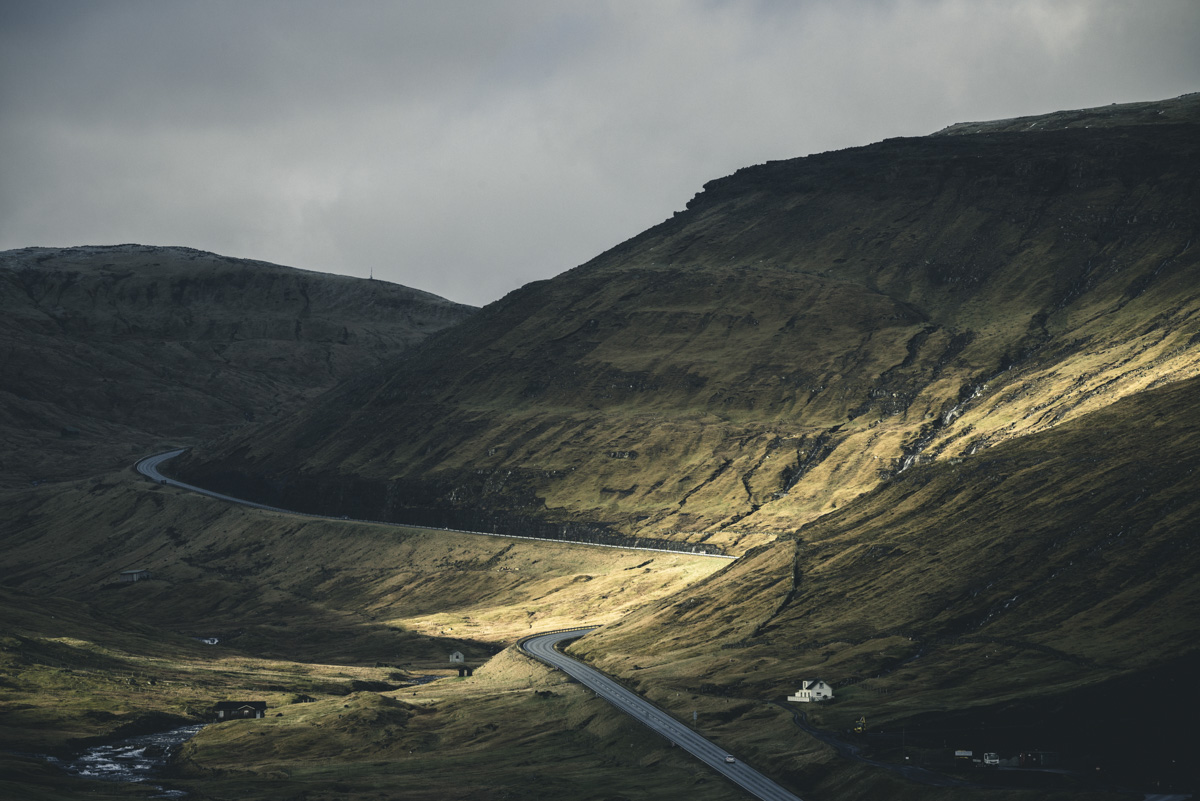 Färöer Inseln, Serpentinenstraße durch sonnenbeschienenes Bergtal, Goldenes Licht im Hochland - Landschaftsfotografie