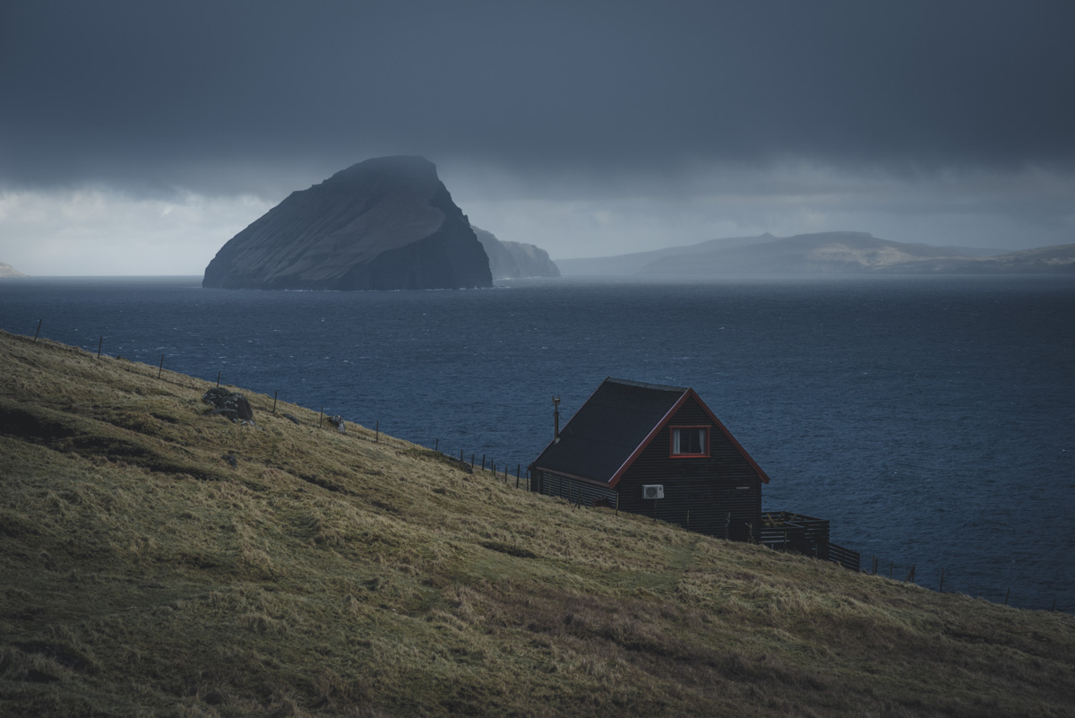 Färöer Haus, Rotes Holzhaus am Fjord mit Felsinsel und Sturmhimmel, Dramatisch - Landschaftsfotografie Nordatlantik
