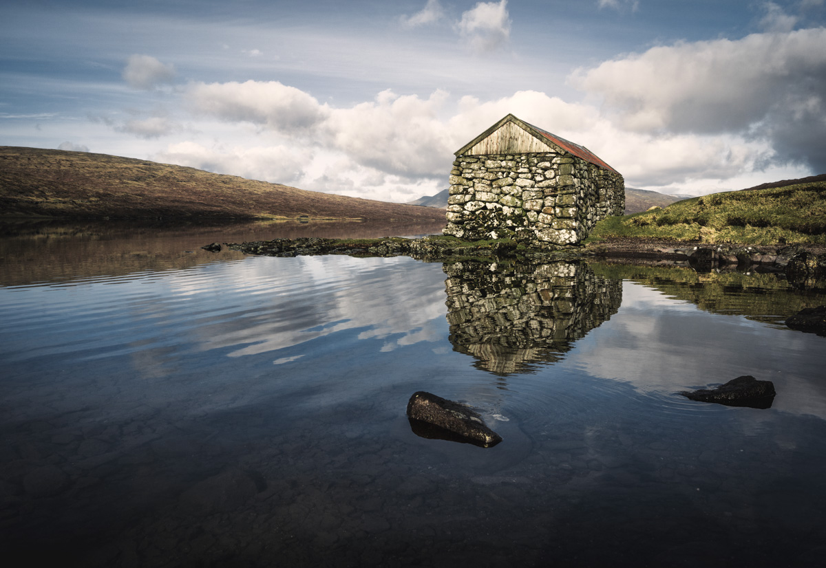 Vágar Bootshaus, Steinerne Hütte am See mit Wolkenspiegelung und Steinen, Malerisch - Landschaftsfotografie Färöer