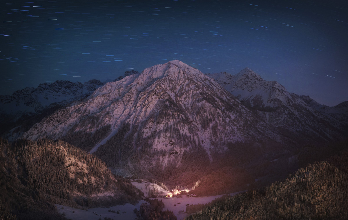 Winternacht über Hinterstein, Sternspuren über dem verschneiten Breitenberg und Rotspitz, Sternenregen über dem Bergdorf