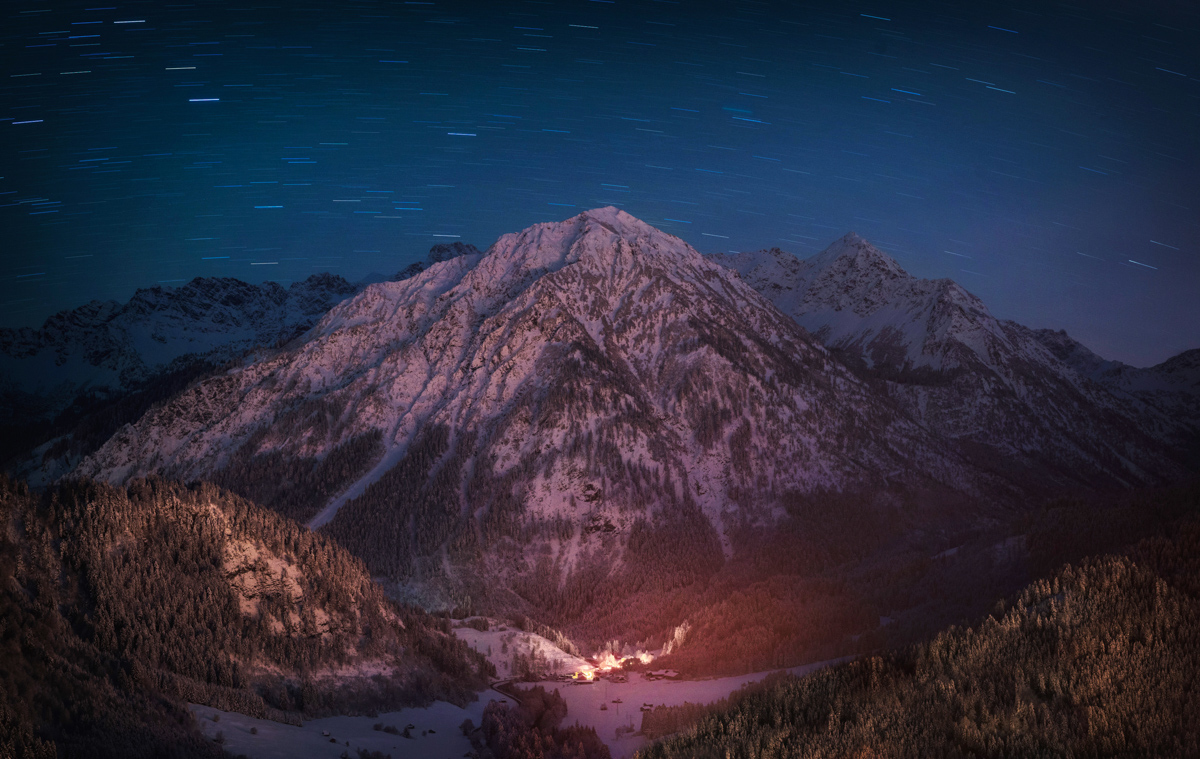 Sternspuren über Breitenberg und Rotspitz bei Hinterstein, Verschneites Bergtal mit leuchtendem Dorf Bruck, Winterliche