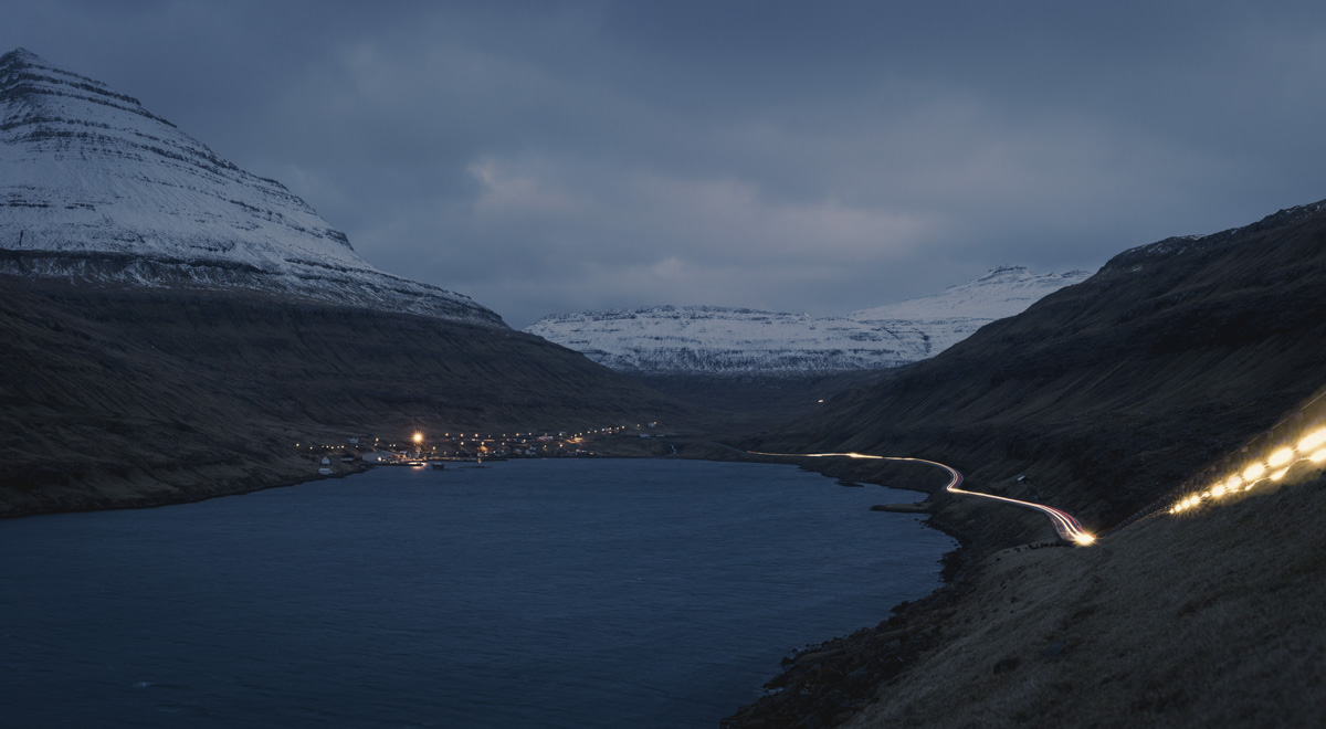 Färöer Dämmerung, Beleuchtetes Dorf am Fjord mit Lichtspuren und schneebedeckten Bergen, Atmosphärisch