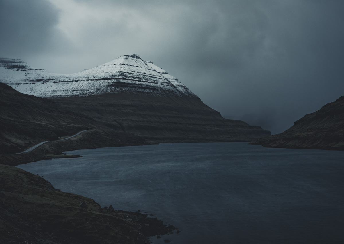 Färöer Pyramidenberg, Schneebedeckter Schichtberg über dunklem Fjord unter Sturmhimmel, Düster - Landschaftsfotografie