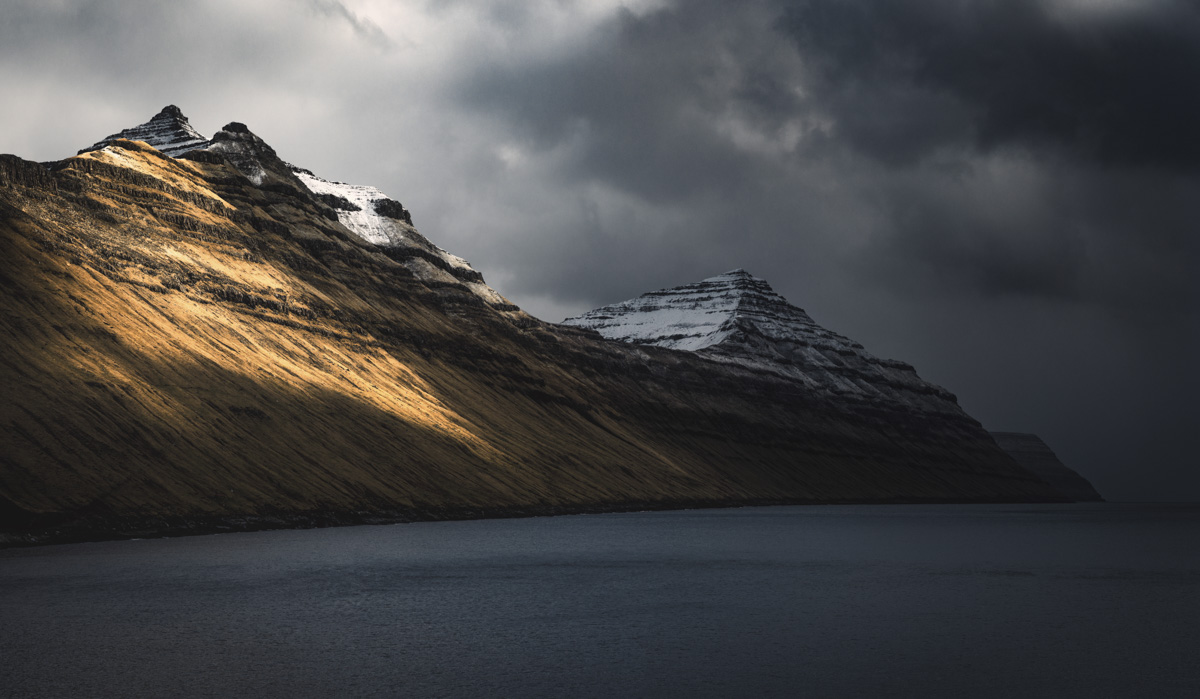 Färöer, Goldenes Streifenlicht auf Schichtbergen über dunklem Fjord, Dramatische Lichtstimmung - Bergfotografie Färöer-Inseln