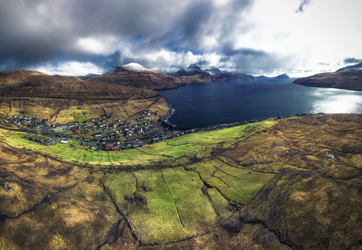 Färöer, Dorf im Talkessel zwischen Bergen und Fjord aus der Luft, Dramatische Insellandschaft - Drohnenfotografie