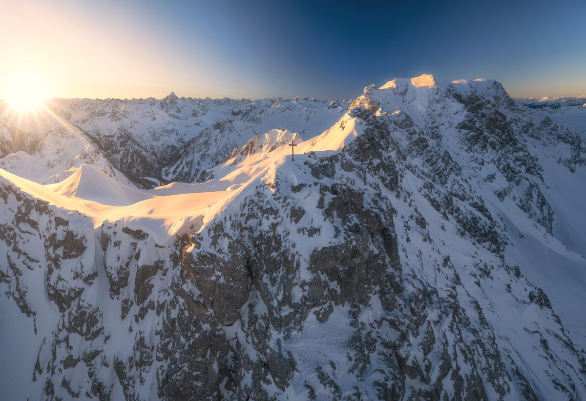 Kleiner Daumen und Hochvogel im winterlichen Morgenglühen, Sonnenaufgang über dem verschneiten Gipfelgrat mit Gipfelkreuz