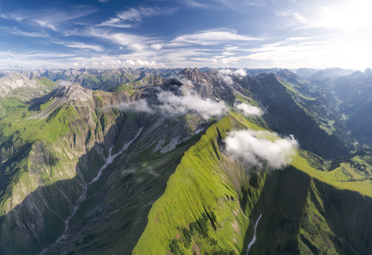 Krottenkopf und Höfats aus der Luft im Frühsommer, Saftig grüne Bergwiesen mit Wolkenfetzen über Trettach und Stillach bei