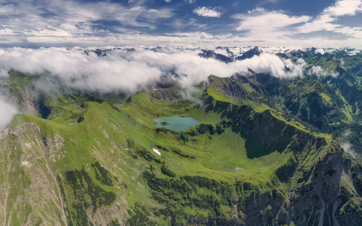 Schrecksee aus der Luft im Sommer, Türkiser Bergsee inmitten grüner Bergwiesen mit Wolkenfetzen bei Hinterstein