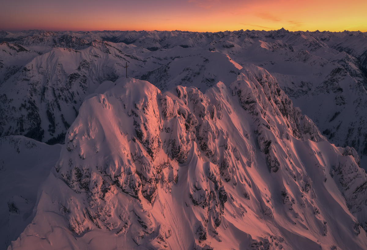 Rauhorn mit Gipfelkreuz im rosafarbenen Alpenglühen, Verschneite Bergkette mit Hochvogel im Hintergrund bei Sonnenuntergang