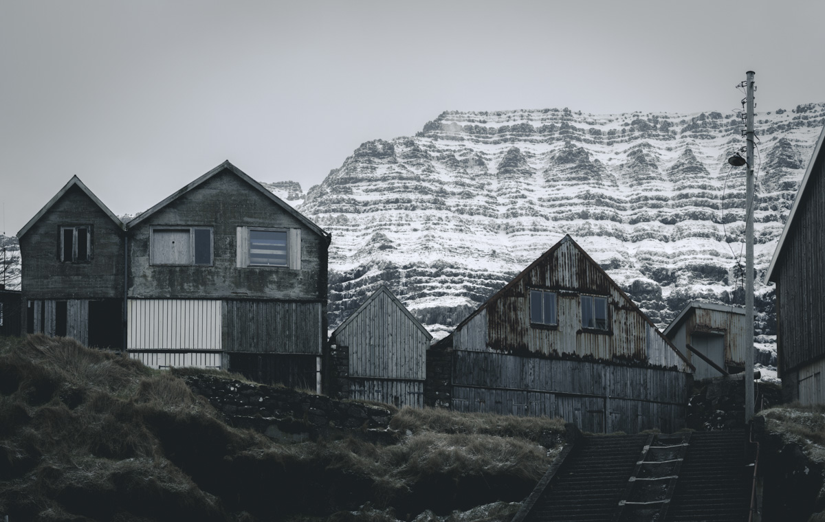 Färöer, Holzhäuser vor verschneitem Schichtberg im Winter, Nordische Dorfarchitektur - Architekturfotografie Färöer-Inseln