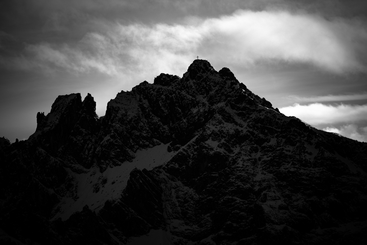 Gipfelkreuz in der Silhouette, Schroffer Berggipfel im Gegenlicht bei Oberstdorf, Winterliche Bergdramatik in Schwarzweiß