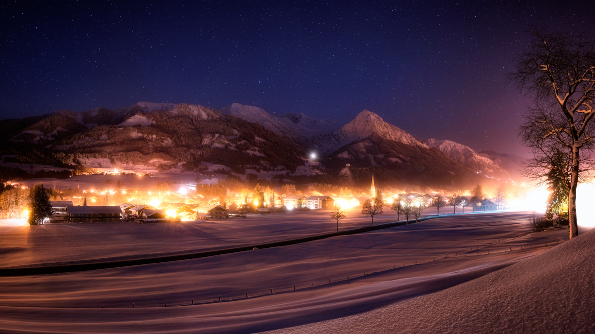 Oberstdorf bei Winternacht im Schnee, Beleuchtetes Allgäuer Bergdorf mit Kirchturm unter Sternenhimmel, Weihnachtspanorama