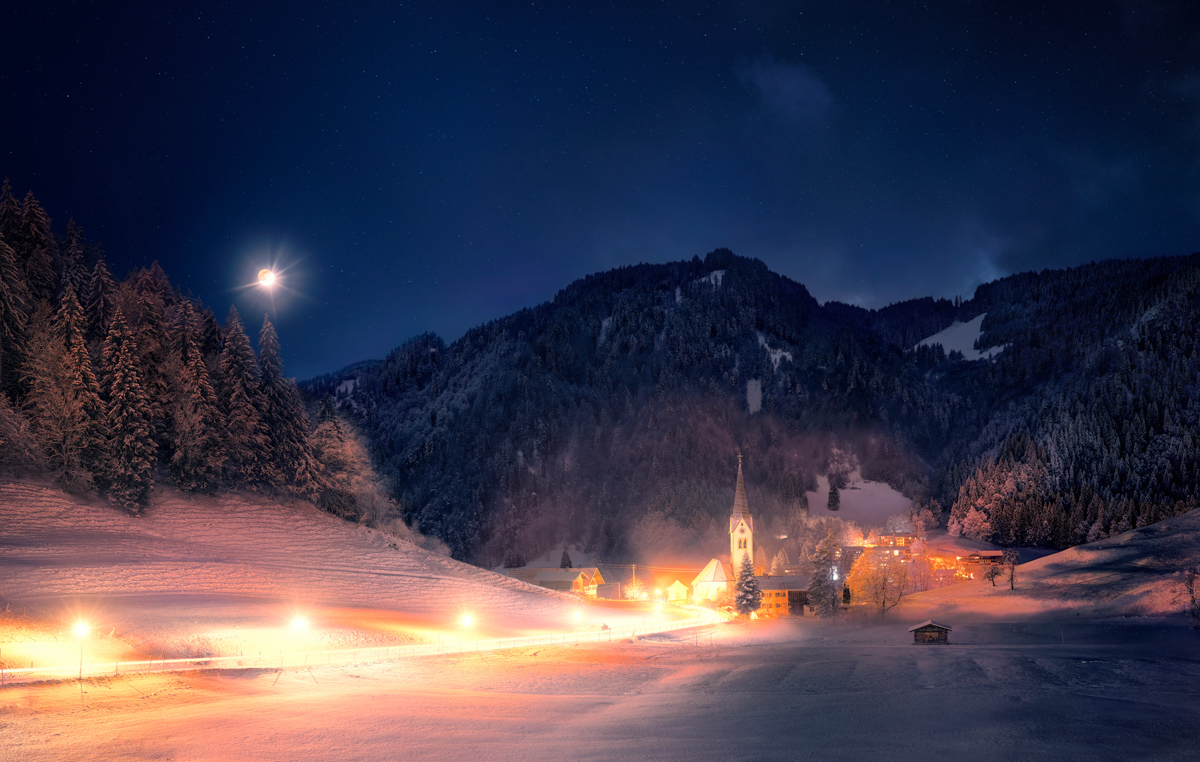 Kapelle in Tiefenbach bei Mondschein, Verschneites Allgäuer Bergdorf mit leuchtender Kirche und Tannen, Weihnachtliche