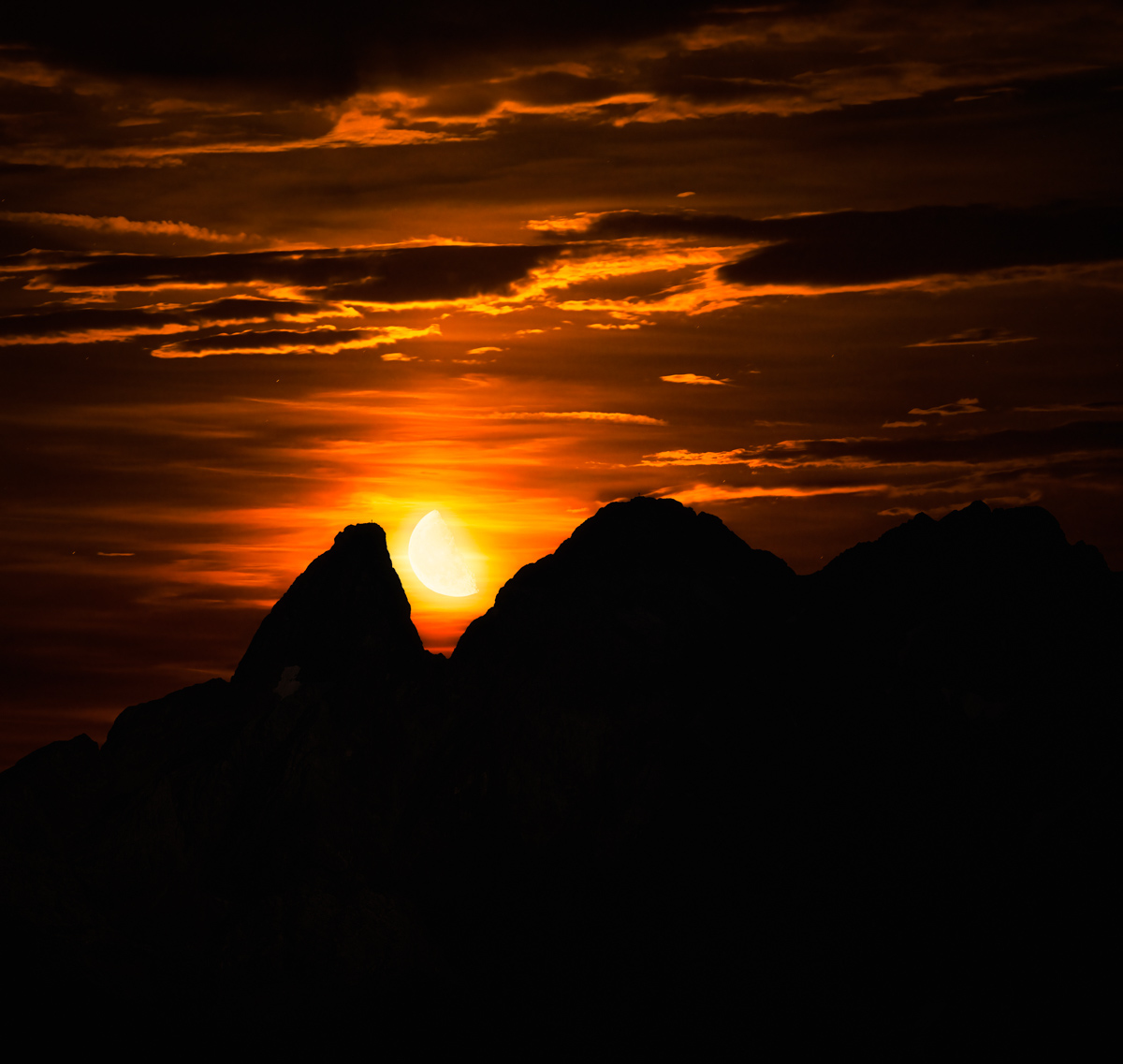 Monduntergang hinter Allgäuer Berggipfeln bei Oberstdorf, Glutroter Himmel mit dramatischen Wolken über Bergsilhouetten