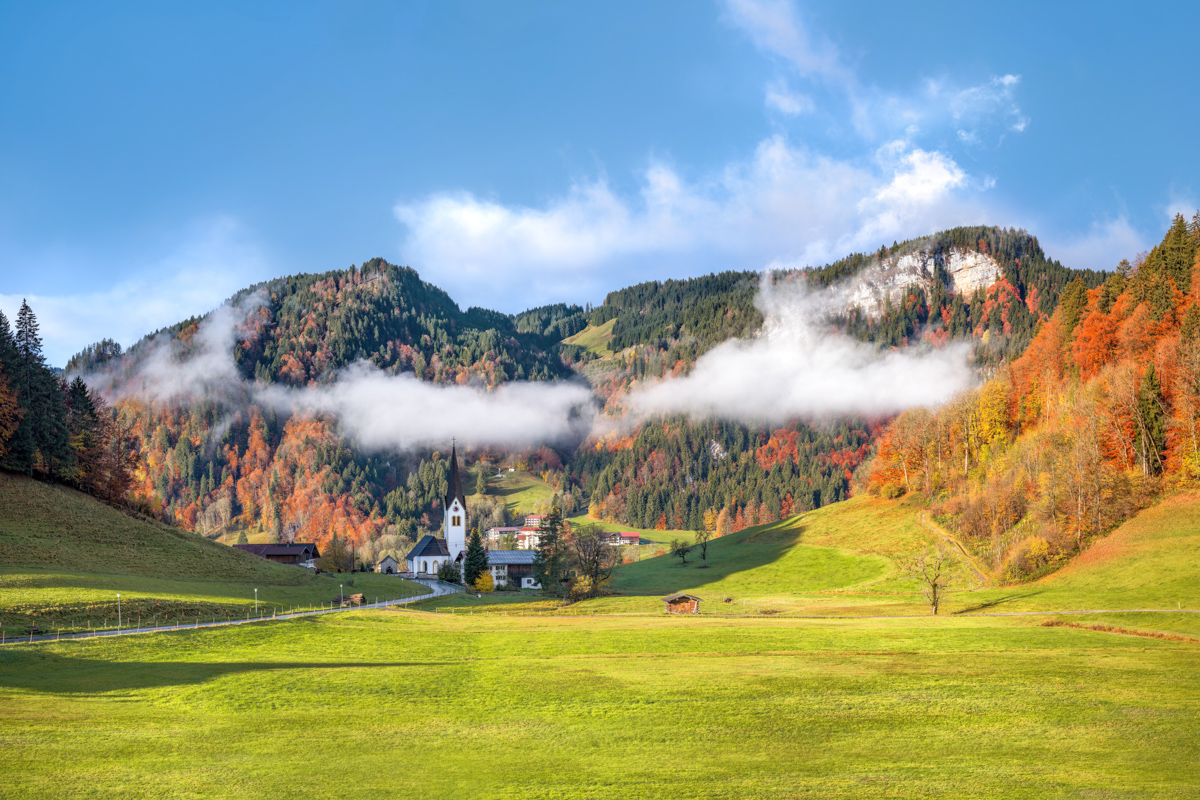 Tiefenbach bei Oberstdorf, Herbstliches Bergdorf mit Kirche vor bunten Laubwäldern und Nebelfahnen, Goldener Oktober im