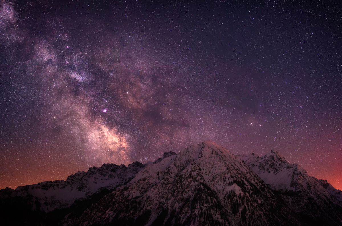 Milchstraße über verschneitem Berggipfel bei Hindelang, Violett-orangefarbener Galaxiehimmel mit Sternschnuppe