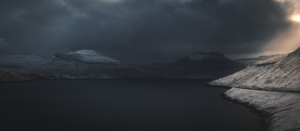 Färöer Fjord Winter, Verschneite Berge am dunklen Fjord mit Lichtstrahl durch Wolken, Dramatisch - Landschaftsfotografie