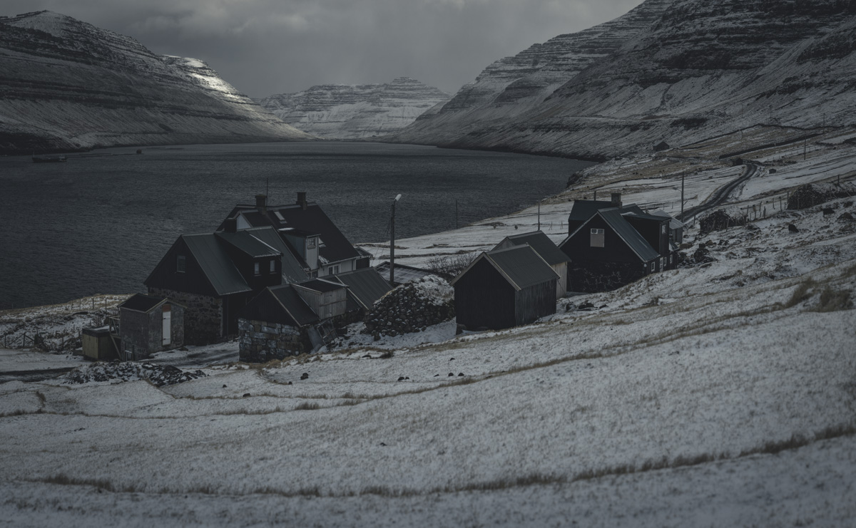Färöer Winterdorf, Verschneites Fjorddorf mit dunklen Holzhäusern vor Schichtbergen, Nordisch - Landschaftsfotografie