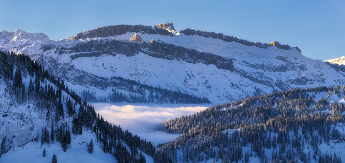 Verschneite Bergwand bei Oberstdorf, Nebelmeer im Tal mit Winterwald und blauem Himmel, Winterpanorama Oberallgäu