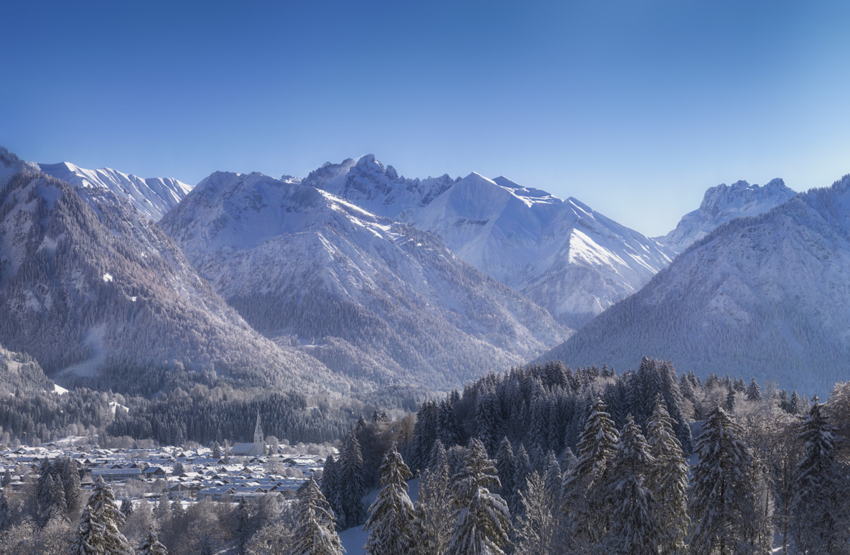 Oberstdorf im Winterkleid mit Kirchturm und Bergpanorama, Verschneites Alpendorf unter blauem Himmel, Allgäu