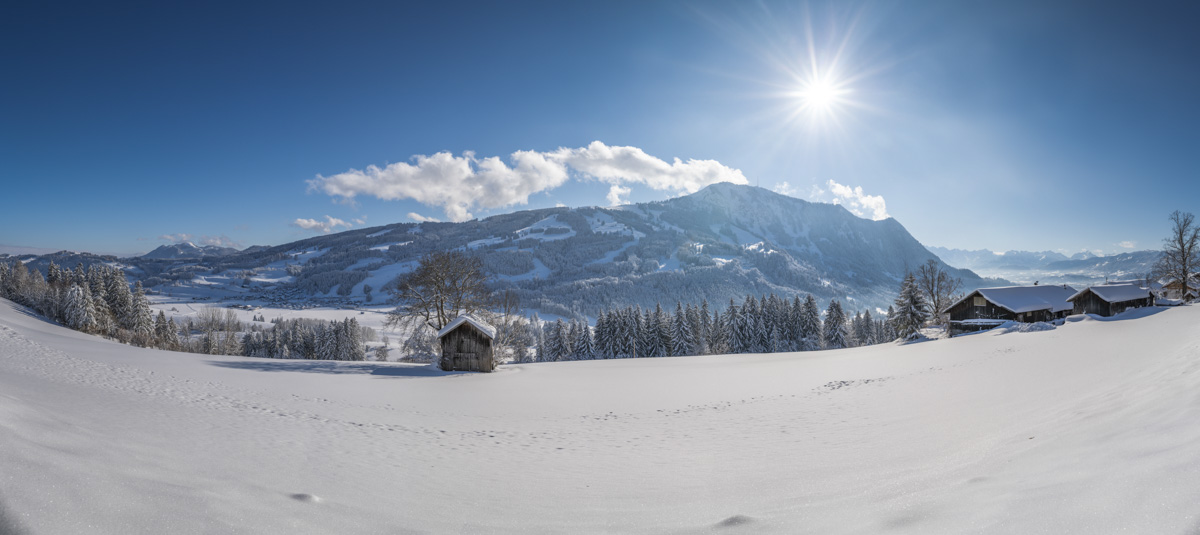 Grünten bei Rettenberg mit Holzhütten im Winter, Sonnenstern über verschneiter Berglandschaft, Winterzauber Oberallgäu